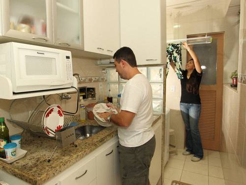 Lúcio Vieira, na cozinha, e Hosana Sauerbron, na área, nas tarefas domésticas. Foto: Carlos Ivan / Agência O Globo. 